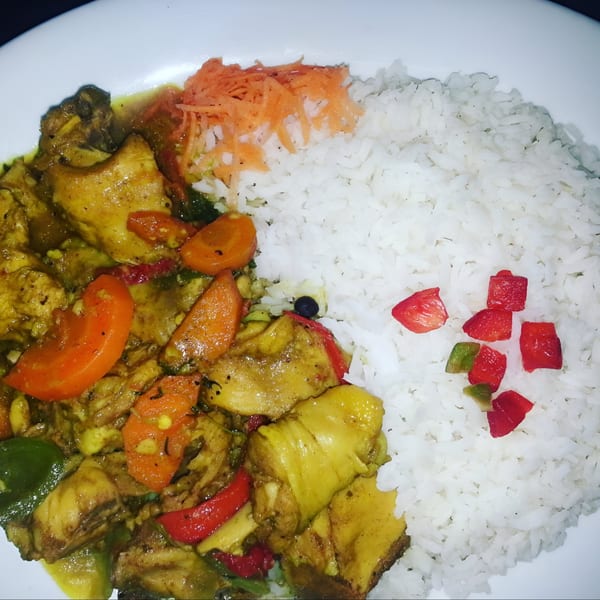Curried chicken with carrots and bell peppers, served with white rice and shredded carrots.