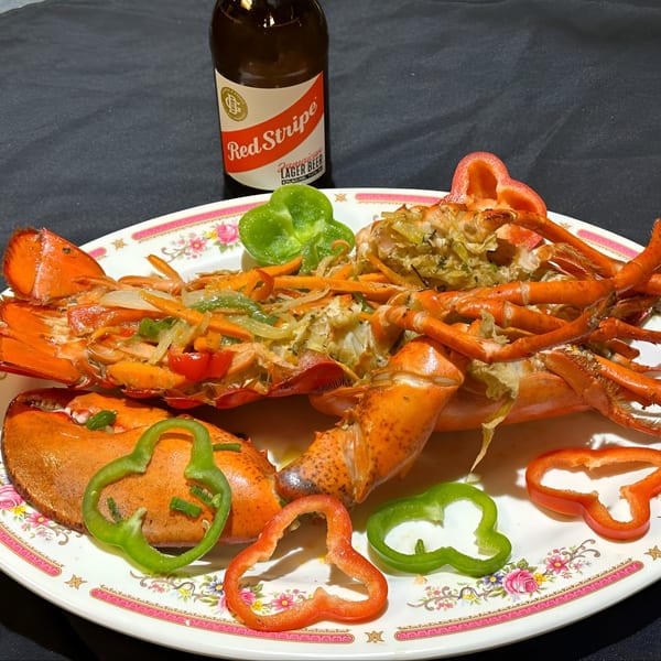 A whole Jamaican-style lobster with vegetables and a Red Stripe beer on a floral plate.