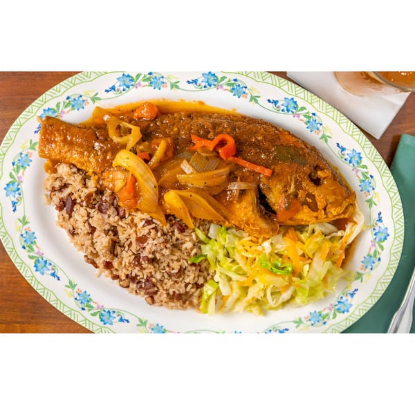 Whole fried fish with brown sauce, rice and peas, and shredded cabbage on a floral plate.