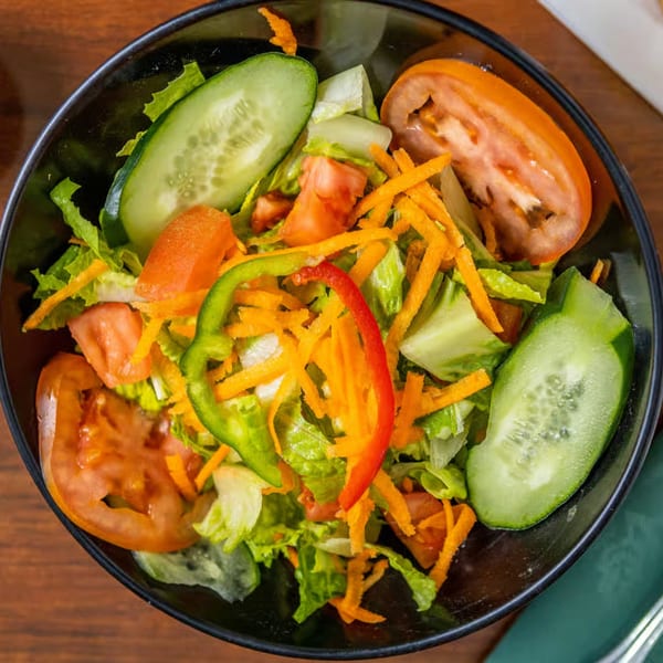 A vibrant side salad with lettuce, tomatoes, cucumbers, shredded carrots, and bell peppers in a black bowl.