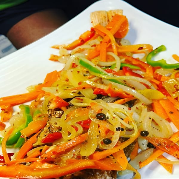 Close-up of Jamaican escovitch fish topped with colorful pickled vegetables on a white plate.